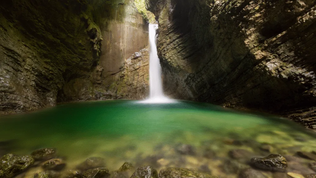 Kozjak Waterfall cascading into a hidden emerald pool surrounded by cave-like rock walls