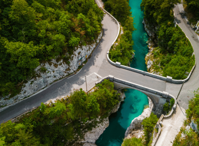 Aerial view of Napoleon Bridge crossing the Soča River with winding roads and forest