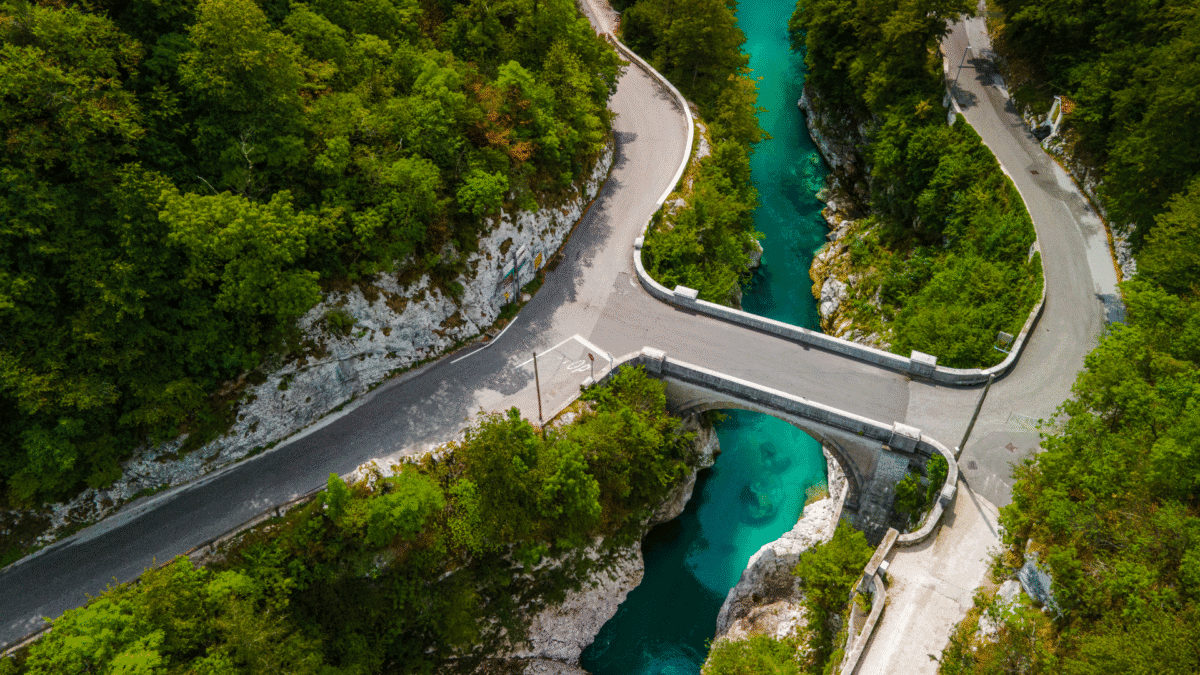 Aerial view of Napoleon Bridge crossing the Soča River with winding roads and forest