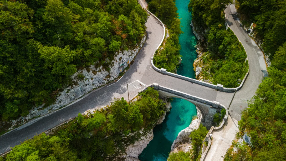Aerial view of Napoleon Bridge crossing the Soča River with winding roads and forest
